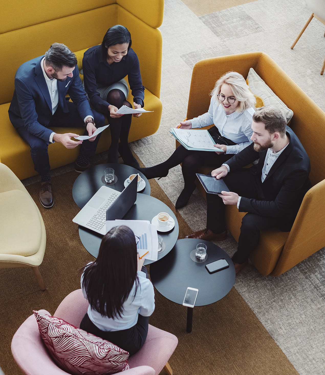 Photo of five smiling people sitting on couches discussing some paperwork.